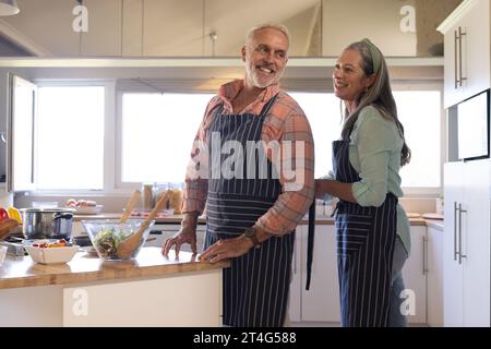Heureux couple caucasien senior portant tablier dans la cuisine à la maison Banque D'Images