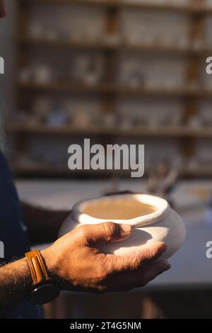 Gros plan des mains de potier biracial senior tenant le vase d'argile dans l'atelier de poterie Banque D'Images
