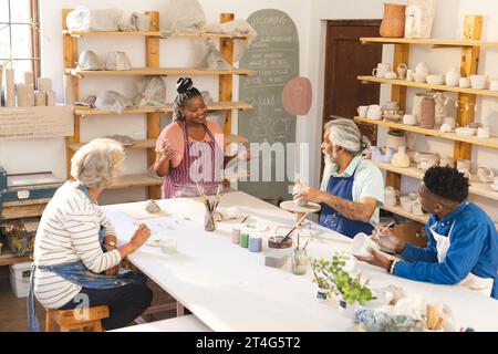 Heureux groupe diversifié de potiers vitrant des cruches en argile et discutant dans le studio de poterie Banque D'Images