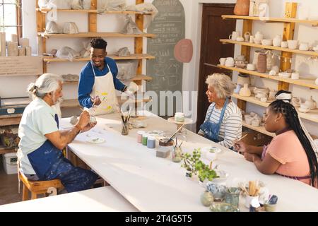 Heureux groupe diversifié de potiers vitrant des cruches en argile et discutant dans le studio de poterie Banque D'Images