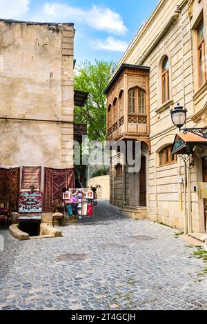 Vue sur une rue pavée typique, générique, avec balcon en bois et une boutique vendant des textiles. Dans la vieille ville de Bakou, Azerbaïdjan. Banque D'Images