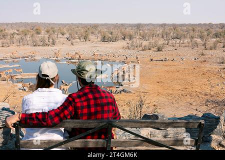 Vue arrière d'un jeune couple observant des animaux dans la savane africaine, parc national d'Etosha, Namibie Banque D'Images