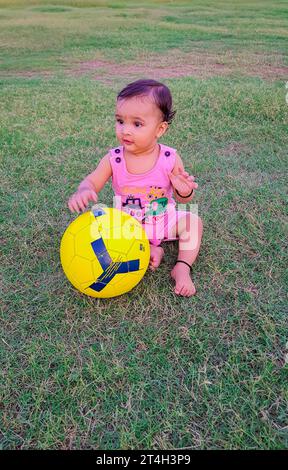 bébé mignon jouant avec le football sur le terrain d'herbe verte sous un angle différent Banque D'Images