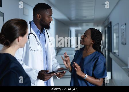 Divers médecins masculins et féminins discutant du travail, en utilisant la tablette dans le couloir à l'hôpital Banque D'Images