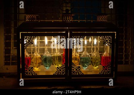 Une menorah Hanukkah utilisant des fioles en verre et des bougies de parafin colorées brûle brillamment dans une boîte de fenêtre à Jérusalem pendant la célébration du Festival o Banque D'Images