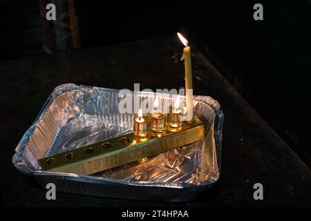 Une bougie de cire sert de shamash ou bougie auxiliaire dans une menorah Hanukkah avec trois lumières d'huile brûlantes et inscrit avec les mots hébreux, 'These ca Banque D'Images