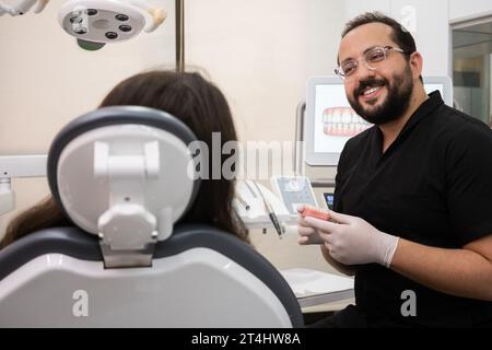 Dentiste souriant avec barbe écoute la patiente se plaindre de maux de dents pendant le rendez-vous Banque D'Images