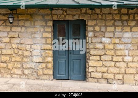 Porte en bois vert vintage avec de petites fenêtres dans un mur en pierre jaune, vue de face, texture de photo de fond Banque D'Images