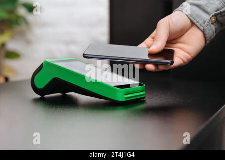 Homme payant la facture via smartphone en utilisant la technologie NFC dans un magasin. Client masculin payant par téléphone mobile en utilisant la technologie sans contact. Gros plan de la main de l'homme faisant le paiement mobile dans le magasin Banque D'Images