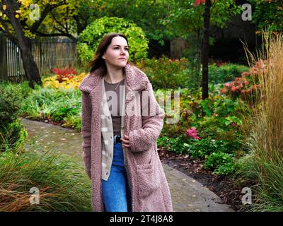 Jeune femme avec les cheveux bruns de longueur d'épaule marchant le long d'un chemin un jour d'automne dans les jardins à York Yorkshire Angleterre Banque D'Images