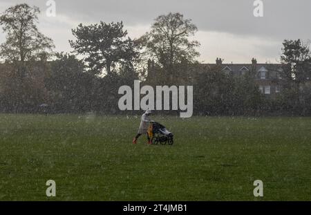 Autumn Rain Showers, Royaume-Uni Une femme se fraie un chemin à travers les fortes averses de pluie alors qu'elle pousse sa poussette d'enfants à travers un terrain de loisirs sur elle pour aller chercher l'école. 31 octobre 2023 Wimbledon, Sud-Ouest de Londres, Angleterre, Royaume-Uni crédit : Jeff Gilbert/Alamy Live News Banque D'Images