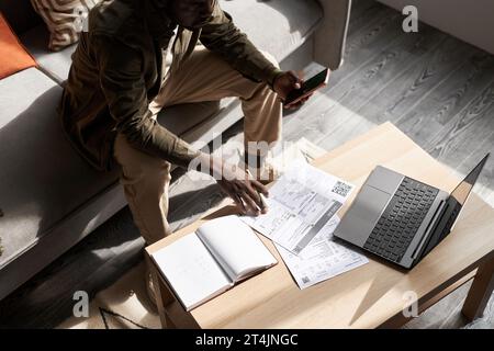 Portrait à grand angle de l'homme adulte noir faisant des impôts à la maison dans la lumière du soleil avec des documents financiers sur la table, espace de copie Banque D'Images