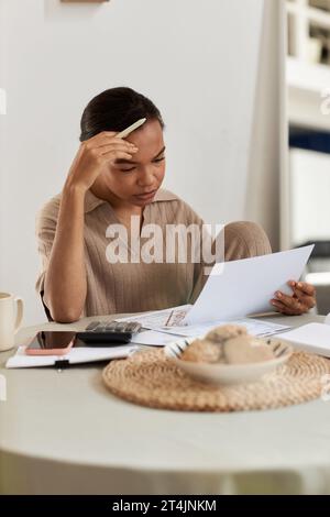 Portrait vertical d'une jeune femme noire troublée faisant des impôts à la maison et lisant des documents bancaires Banque D'Images