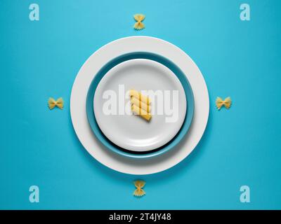Pâtes rigatoni non cuites sur une assiette sur fond bleu. Vue de dessus, espace de copie. Concept alimentaire créatif. Banque D'Images