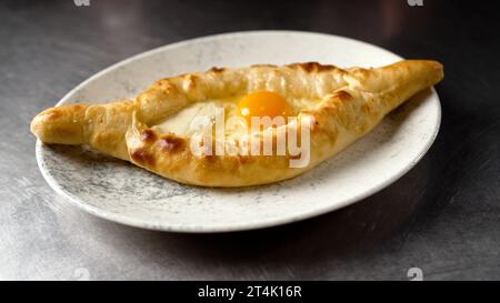 Khachapuri sur une assiette sur la table gros plan. Une assiette avec de délicieux Adjarian khachapuri sur un fond de table sombre. Khachapuri est servi sur une assiette Banque D'Images