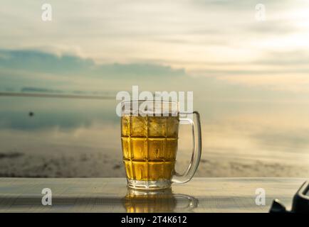 Gros plan un verre de bière est debout sur une table avec la mer floue sur le fond. Bière avec mousse. Coucher de soleil et naturel. Concept alcool et non alcool. Banque D'Images