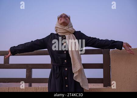 femme portant le hijab et les vêtements islamiques ayant des vacances dans la station avec le sourire sur leur visage et de belles lumières floues en arrière-plan Banque D'Images