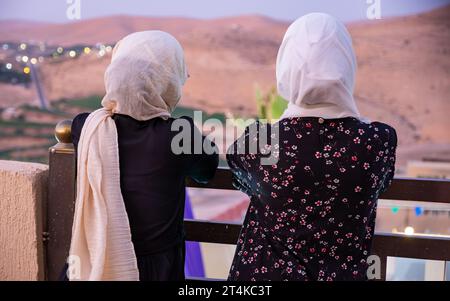 Deux femmes portant le hijab et des vêtements islamiques ayant des vacances dans la station avec le sourire sur leur visage et de belles lumières floues en arrière-plan Banque D'Images