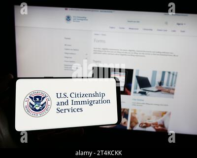Personne tenant un smartphone avec le sceau de l'agence américaine Citizenship and Immigration Services (USCIS) devant le site Web. Concentrez-vous sur l'affichage du téléphone. Banque D'Images