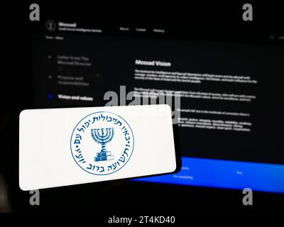 Personne tenant un téléphone portable avec le logo de l'agence de renseignement nationale israélienne Mossad devant la page web. Concentrez-vous sur l'affichage du téléphone. Banque D'Images