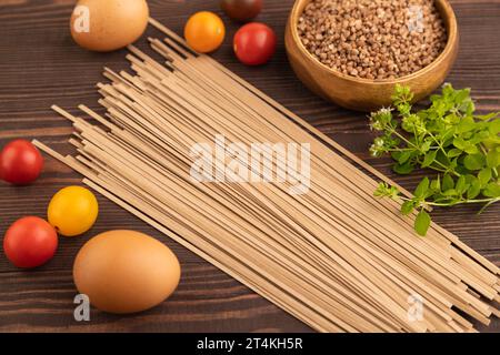 Nouilles soba de sarrasin japonaises avec tomates, œufs, épices, herbes sur fond de bois brun. Vue latérale, gros plan, mise au point sélective. Banque D'Images