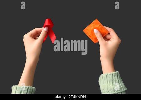 Mains féminines avec ruban rouge et préservatif sur fond noir. Concept de la Journée mondiale du sida Banque D'Images