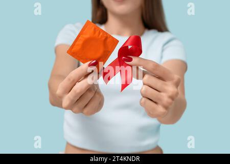 Femme avec ruban rouge et préservatif sur fond bleu, gros plan. Concept de la Journée mondiale du sida Banque D'Images