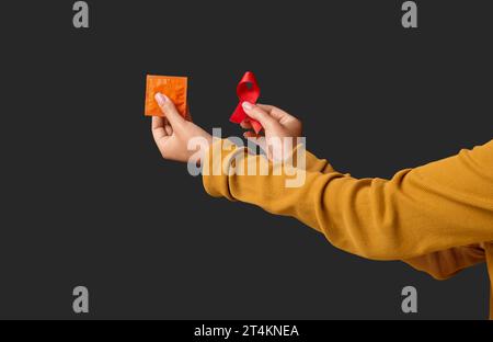 Mains féminines avec ruban rouge et préservatif sur fond noir. Concept de la Journée mondiale du sida Banque D'Images