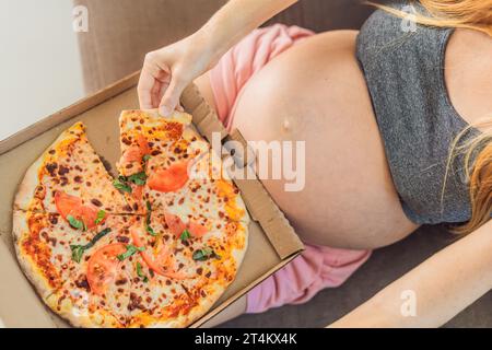 Une femme enceinte apprécie une tranche de pizza, savourant un moment de plaisir tout en satisfaisant son envie d'un régal délicieux et réconfortant. Excité Banque D'Images