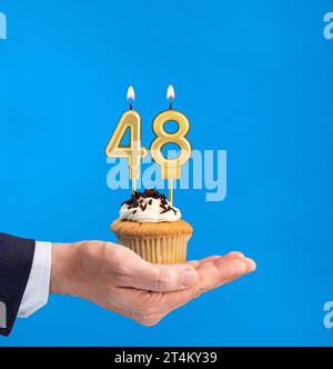 Main livrant cupcake d'anniversaire - bougie numéro 48 sur fond bleu Banque D'Images