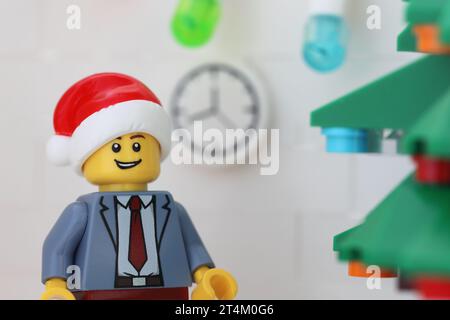 Tambov, Fédération de Russie - 31 octobre 2023 Une minifigurine d'homme d'affaires Lego portant un chapeau de Père Noël et debout à côté d'un arbre de Noël dans son bureau Banque D'Images