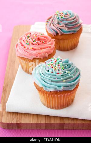 Cupcakes au beurre avec glaçage rose et bleu sur une planche à découper en bois, sur fond rose Banque D'Images