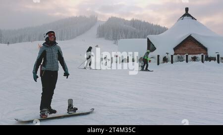 Femme profiter des vacances d'hiver sur la station de ski. Snowboard fille écouter de la musique, et s'amuser, piste de ski, forêt enneigée en arrière-plan. Sport actif. Bukovel, montagnes des Carpates, Ukraine Banque D'Images