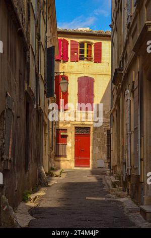 Ruelle dans la ville d'Arles, France, avec un bâtiment aux volets rouges. Banque D'Images