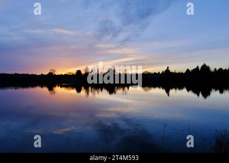 Un lac tranquille se prélasse dans les derniers rayons de soleil alors que le soleil se couche sur l'horizon au loin Banque D'Images