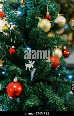 Figurine d'un cerf parmi des boules brillantes colorées accroche sur les branches d'un arbre de Noël Banque D'Images