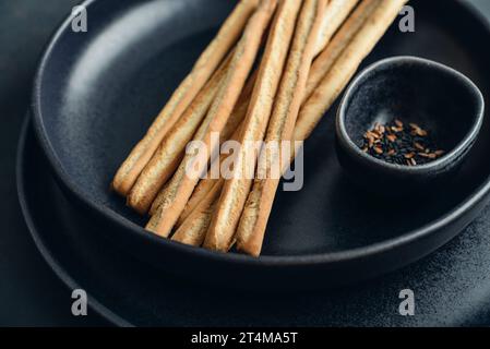 Grissini italiens frais cuits au four sur l'assiette avec des graines de sésame et de lin sur fond noir closeup Banque D'Images