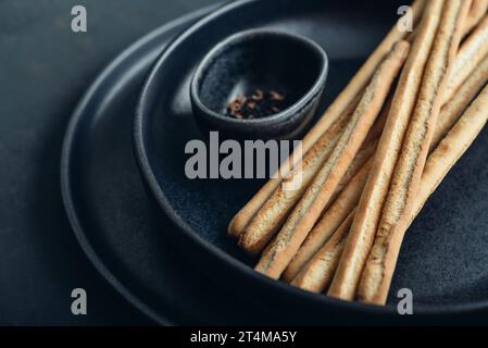 Grissini italiens frais cuits au four sur l'assiette avec des graines de sésame et de lin sur fond noir closeup Banque D'Images