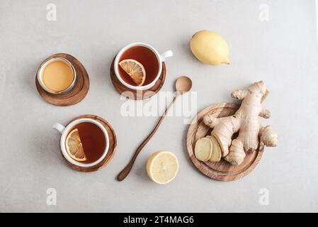 Thé dans une tasse blanche avec citron, racine de gingembre sur la planche à découper et miel sur un fond clair, vue de dessus Banque D'Images