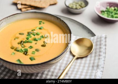 Soupe de citrouille dans un bol avec des graines de citrouille, des oignons verts et des gressins sur un fond clair Banque D'Images