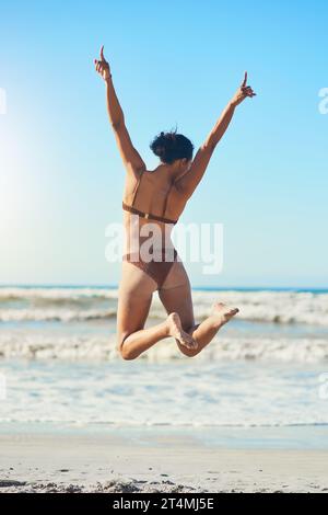 Rien ne vaut une journée ensoleillée sur la plage. Vue arrière d'une jeune femme debout sur la plage. Banque D'Images