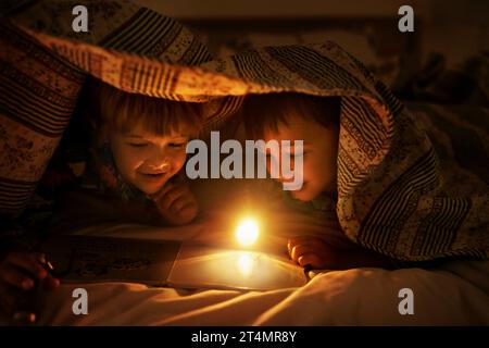 Les frères sont amis pour la vie. Deux jeunes frères coloriant en images alors que sous leur couverture après leur coucher. Banque D'Images