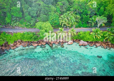 Drone oeil d'oiseau de la plage de baie lazare, pierres de granit, eau turquoise, cocotiers, route publique asphaltée, journée ensoleillée, Mahé Seychelles Banque D'Images