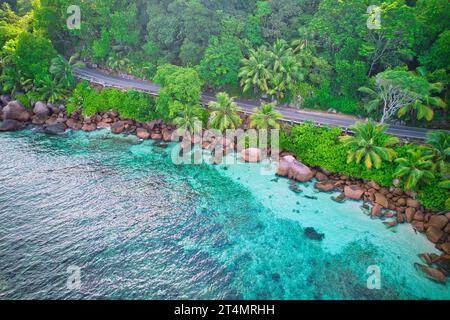 Drone oeil d'oiseau de la plage de baie lazare, pierres de granit, eau turquoise, cocotiers, route publique asphaltée, journée ensoleillée, Mahé Seychelles Banque D'Images