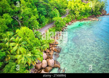 Drone oeil d'oiseau de la plage de baie lazare, pierres de granit, eau turquoise, cocotiers, route publique asphaltée, journée ensoleillée, Mahé Seychelles Banque D'Images