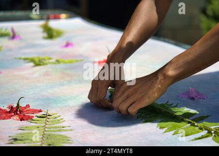 Mains plaçant des feuilles sur le tissu pour des impressions de paréo à l'atelier, Mahé Seychelles Banque D'Images