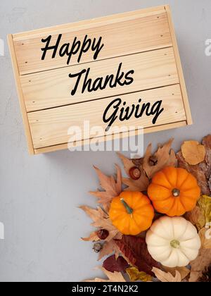 Concept de Thanksgiving. Citrouilles d'automne et feuilles d'automne sur fond texturé gris avec une caisse en bois avec texte de Thanksgiving heureux. Banque D'Images