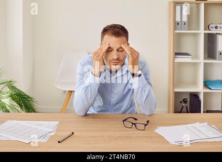 Stressé, fatigué, surmené homme d'affaires souffrant de maux de tête au travail dans le bureau Banque D'Images