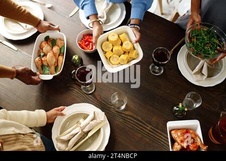 Au-dessus de l'angle des mains des membres de la famille mettant de la nourriture maison sur la table tout en se préparant pour le dîner festif le jour de Thanksgiving Banque D'Images