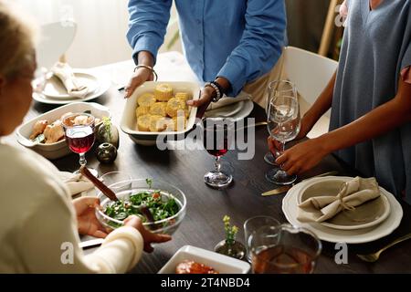 Deux filles aidant leur mère servir la table de fête tout en mettant des verres à vin et un bol de salade de légumes contre la jeune femme avec du maïs cuit au four Banque D'Images